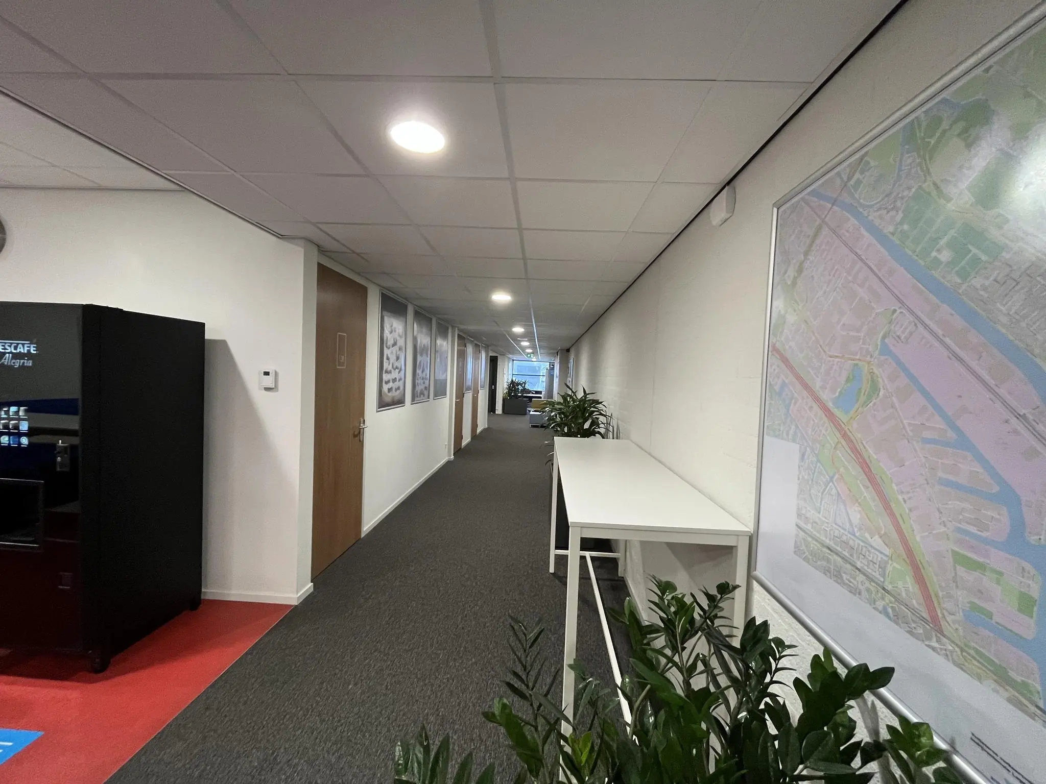 Kantoorhal op de Niels Bohrweg met plattegrond aan de muur, planten, statafel en een koffiemachine.